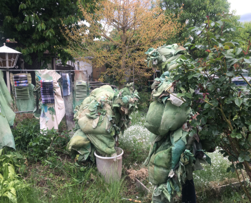 Verkleidete Menschen als Büsche im Kleingarten, kaum zu erkennen